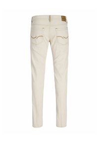 Jean slim beige avec poches arrière, coutures visibles et un patch de marque en cuir marron sur la ceinture, vu de dos.