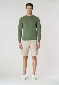 Maglione lavorato a maglia verde oliva con maniche lunghe abbinato a pantaloni cargo beige con tasche laterali, indossato con sneakers bianche.