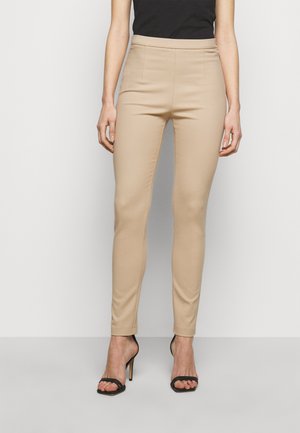 Beige, rekbare stof broek met een slim fit en geen zichtbare zakken, gecombineerd met zwarte hoge hak sandalen en een zwart top.