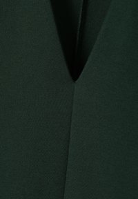 Tissu extensible vert foncé avec une texture lisse. Doté d'un décolleté en V et d'éléments de design superposés. Style minimaliste.