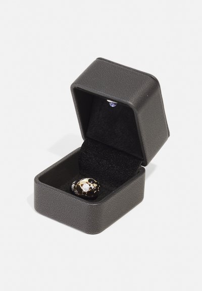 Black textured jewelry box with a shiny gold and black ring featuring diamond accents, resting on black velvet lining.