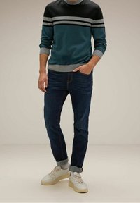 Herrtröja i teal och svart med rund halsringning, med horisontella grå ränder, kombinerad med mörkblåjeans och vita sneakers. Avslappnad passform.