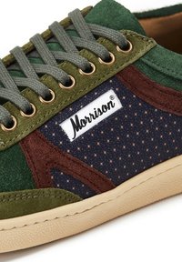 Zapatillas de ante verde y marrón con paneles de tela azul marino con patrones de estrellas, ojales dorados y cordones grises. Logo "Morrison" mostrado en el lateral.