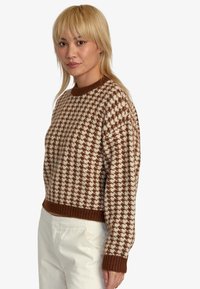 Suéter de pata de gallo en tonos marrón y crema con cuello redondo y puños acanalados, que presenta un corte cropped y una textura suave.