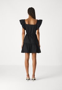 Rochie neagră din bumbac cu un corset ajustat, mâneci flared cu volane și o fustă evazată stratificată. Textură netedă cu o culoare solidă pe toată suprafața.