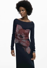 Hosszú ujjú ruha tengerészkék anyagból, piros-fehér hullámos csíkmintával az elején, csónaknyakkivágással és testhezálló sziluettel.