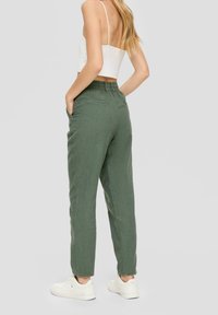 Grüne Leinenhosen mit entspannter Passform, elastischem Bund und Seitentaschen, kombiniert mit weißen Sneakers vor einem hellen Hintergrund.