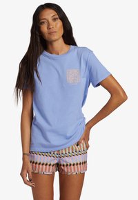 Camiseta de algodón azul claro con un estampado en el pecho de patrones florales, combinada con pantalones cortos estampados en colores pastel y formas geométricas.