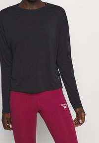Black long-sleeve shirt with a relaxed fit, featuring a round neckline and subtle side detail, paired with fitted burgundy leggings.