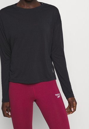 Black long-sleeve shirt with a relaxed fit, featuring a round neckline and subtle side detail, paired with fitted burgundy leggings.