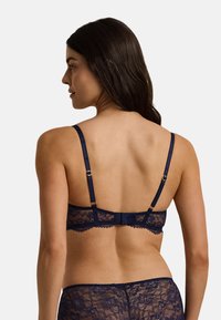 Marinblå spets-bh med justerbara satinband, blommönster, vågkantade kanter och guldfärgad spänne bak.