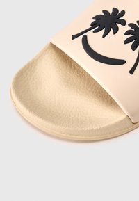 Beige slide sandal with textured sole, featuring black palm tree and smile graphics on the strap. Made from soft, flexible material.