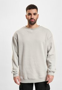 Sudadera oversized gris claro con cuello redondo, hombros caídos y puños acanalados. Textura suave y detalles de costura mínimos.