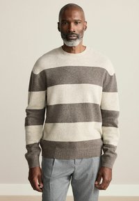 Striped sweater in cream and shades of brown, made of soft knit material, with a crew neckline and ribbed cuffs and hem.