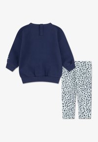 Granatowy sweatshirt z prążkowanymi mankietami i dolnym brzegiem, połączony z jasnymi legginsami z czarno-szarym wzorem w panterkę.