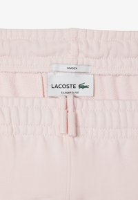 Lichtroze tapered fit shorts met een elastische tailleband, voorzien van Lacoste branding en twee trekkoord toggles. Unisex ontwerp.