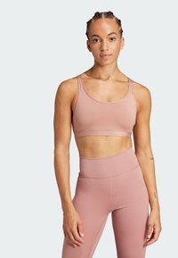 Sujetador deportivo de color rosa claro con una tela suave y elástica; presenta tirantes anchos y una banda ribeteada debajo del busto; combinado con leggings a juego.