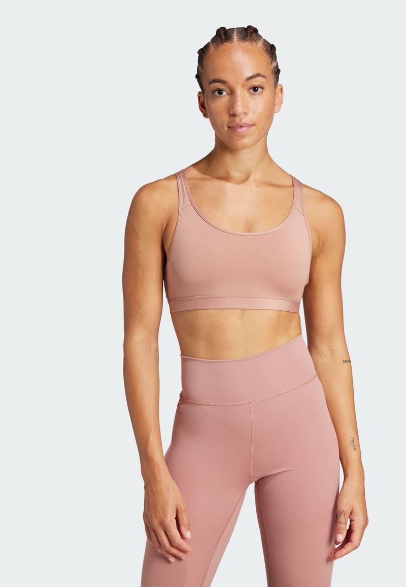 Sujetador deportivo de color rosa claro con una tela suave y elástica; presenta tirantes anchos y una banda ribeteada debajo del busto; combinado con leggings a juego.