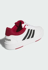 Białe trampki z czerwonymi akcentami, czarnymi paskami po bokach, wyprofilowanym czerwonym kołnierzem i językiem, teksturowanym materiałem i logo na pięcie. Okrągły kształt noska.