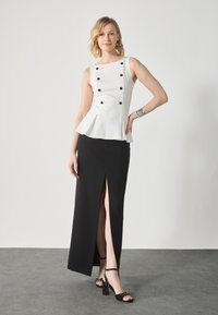 Biele peplum top s čiernymi gombíkmi, v kombinácii s čiernou sukňou s rozparkom po stehná a čiernymi sandálmi na vysokom opätku s mašľovými detailmi.