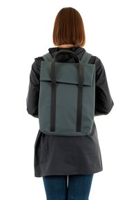 Mochila rectangular verde con correas negras, hecha de material texturizado, que presenta un cierre de solapa y un diseño minimalista.