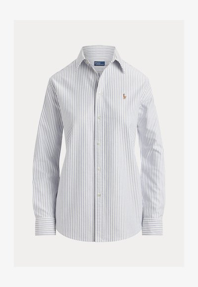 Hvid skjorte med tynde, lodrette blå striber, lange ærmer, spids krave og lille broderet logo på brystet.