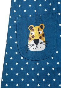 Niebieska tkanina w białe kropki, z kieszenią ozdobioną haftem przedstawiającym żółto-brązową twarz lamparta.