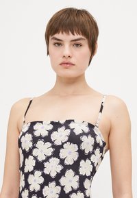 Blumenkleid mit taillierter Passform, dünnen Trägern, dunklem Hintergrund und großen cremefarbenen Blumen mit lila Mittelpunkten und Konturen.
