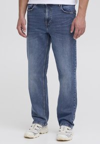 Jeans en denim bleu avec une coupe droite, dotés de poches avant et arrière, d'un léger froissement et de détails de couture contrastés.