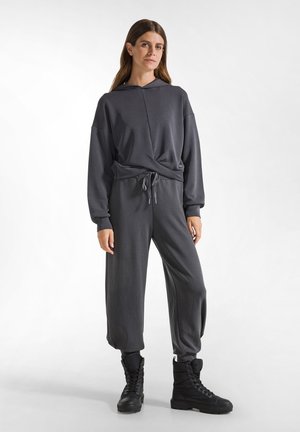 Grijze loungewear set met een hoodie met een trekkoord in de taille en comfortabele broek. Gecombineerd met zwarte, hoge laarzen.