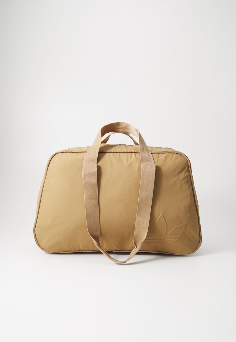Saco duffel bege com duas alças de tecido, textura suave, fecho com zíper, forma oval e um logótipo em relevo discreto de um dos lados.