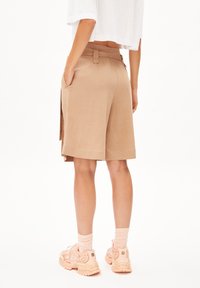 Beige shorts with side pockets and a belt loop feature, paired with pink athletic shoes and light socks, viewed from the back.