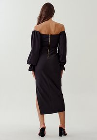 Schwarzes, schulterfreies Kleid mit Puffärmeln, Reißverschlussdetails vorne und seitlichem Schlitz, aus glattem Material gefertigt, körperbetonte Silhouette.