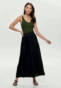 Top verde abbinato a una lunga gonna maxi nera e fluida. L'outfit presenta una vita morbida e una texture soffice. Sandali neri completano il look.