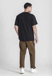 Černé bavlněné tričko s krátkým rukávem, volný střih, kombinované s hnědými zúženými kalhotami a bílými teniskami. Jednoduchý design, bez viditelných log.