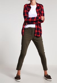 Rood en zwart geruite flanellen shirt over een wit T-shirt, gecombineerd met olijfgroene tapered broek en bruine instapschoenen.