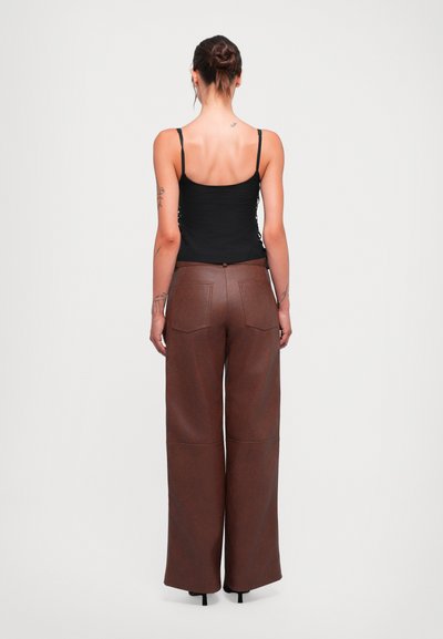 Braune Kunstleder-Hosen mit weitem Bein und hoher Taille, Gesäßtaschen und Knopfverschluss. Enganliegendes Oberteil mit verstellbaren Trägern.
