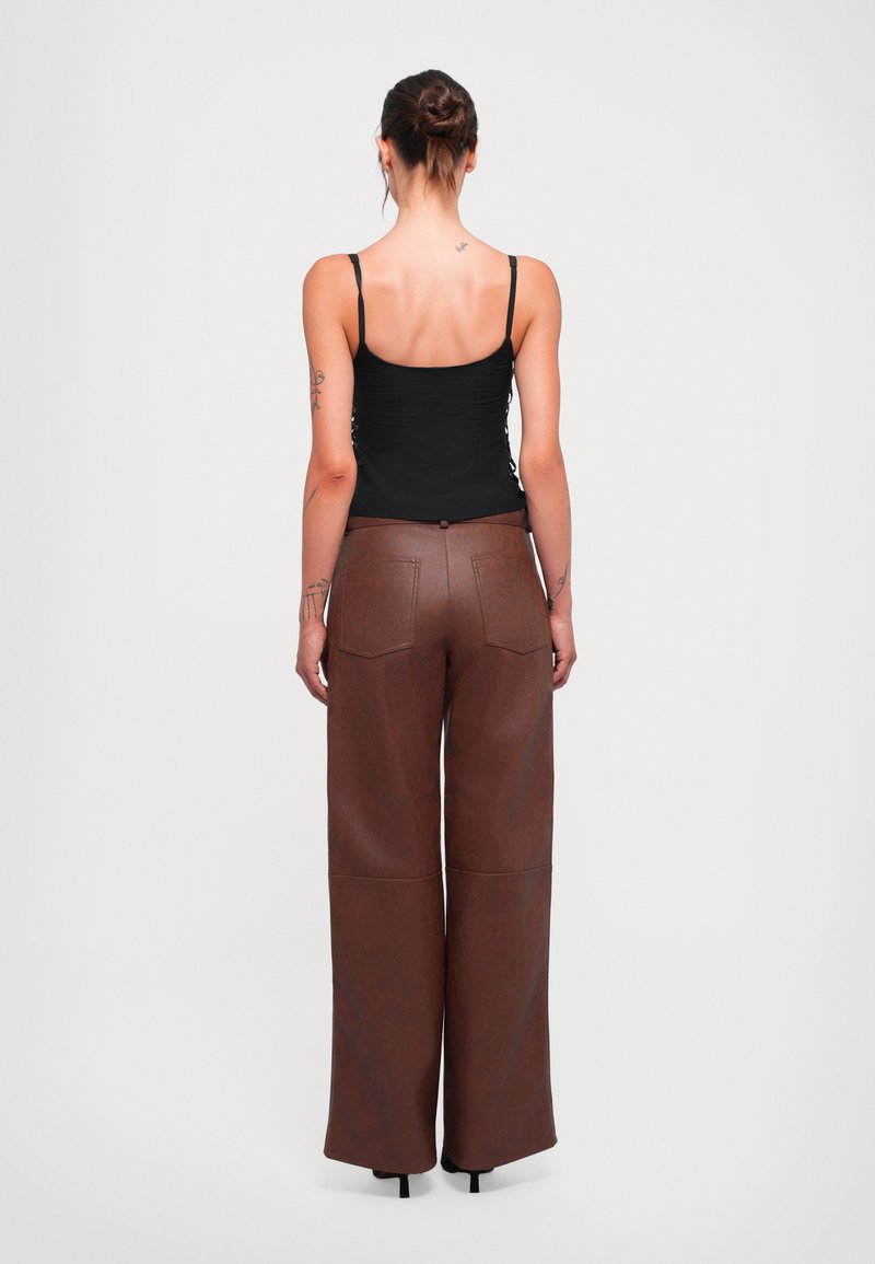 Bruine neplederen broek met wijde pijpen en hoge taille, met achterzakken en een knoopsluiting. Strak aansluitend top met verstelbare bandjes.