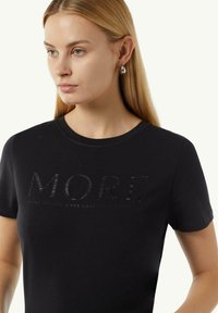 Zwart katoen T-shirt met reliëftekst "MORE" op de voorkant, ronde halslijn en korte mouwen. Zachte textuur met minimale details.
