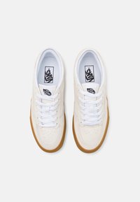 White suede sneakers with a gum rubber sole, flat white laces, and a black Vans logo tag. Perforated toe design for breathability.
