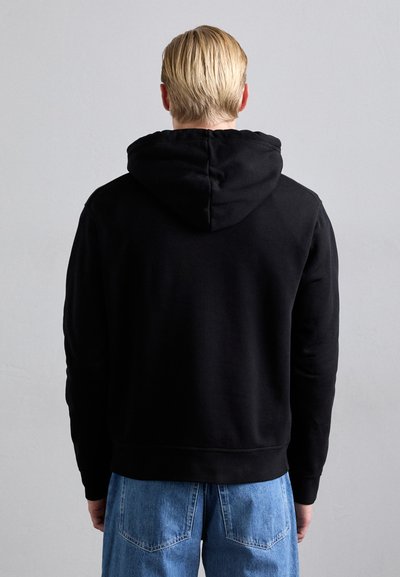 Svart hoodie i mjukt material, med dragsko i huvan, ribbstickade ärmslut och nederkant. Modellen bär ljusblå jeans.