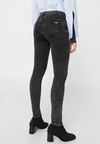 Jeans skinny de mezclilla negra con una textura desgastada, talle alto, dos bolsillos traseros y detalles de costura sutiles, combinados con botines hasta el tobillo.