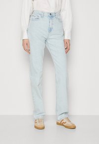 Ljust blå denimjeans med raka ben, med framfickor och en urblekt finish, tillsammans med beige och bruna sneakers.