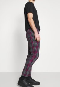Černé tričko spárované s multikolorovými kostkovanými kalhotami v růžových, šedých a černých tónech; slim fit; boční kapsy; nošeno s černými teniskami.