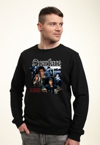 Felpa nera con grafica "Scarface" che presenta immagini dei personaggi e il titolo in bold bianco e rosso. Tessuto morbido e strutturato, vestibilità casual.