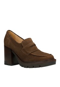 Mocassins à talons en suède marron avec un large détail de bride, un talon épais et une semelle en caoutchouc texturée. Accents cousus le long des bords.