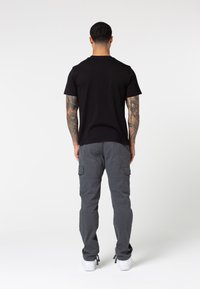Black short-sleeve t-shirt paired with gray cargo pants. T-shirt has a standard fit; pants feature side pockets and a relaxed silhouette.
