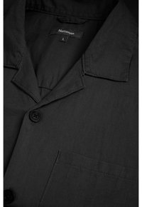 Czarna koszula wykonana z tkaniny plecionej. Posiada kołnierzyk, kieszeń na przodzie oraz zapięcie na guzik z pojedynczym czarnym guzikiem. Metka pokazuje "Matinique" oraz rozmiar L.