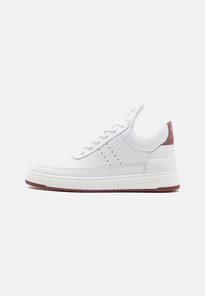 Basket basse en cuir blanc avec lacets blancs, détails perforés sur le côté, et languette de talon ainsi qu’un accent de semelle bordeaux.