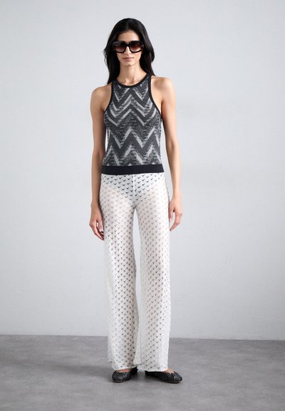Black and white patterned tank top with a round neckline, paired with wide-leg white pants featuring a lace-like texture and black accents.
